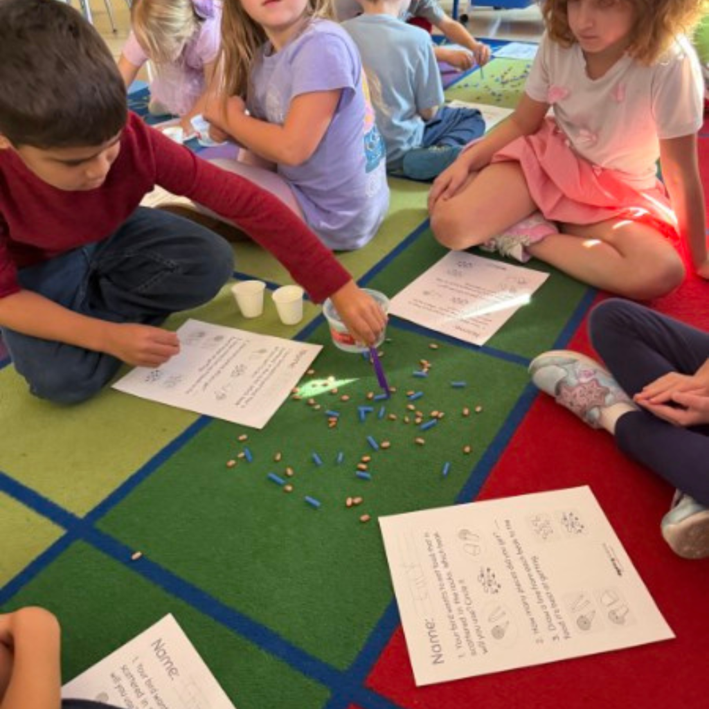 Elementary students sitting on a colorful classroom rug smiling during a group lesson with an interactive display board.