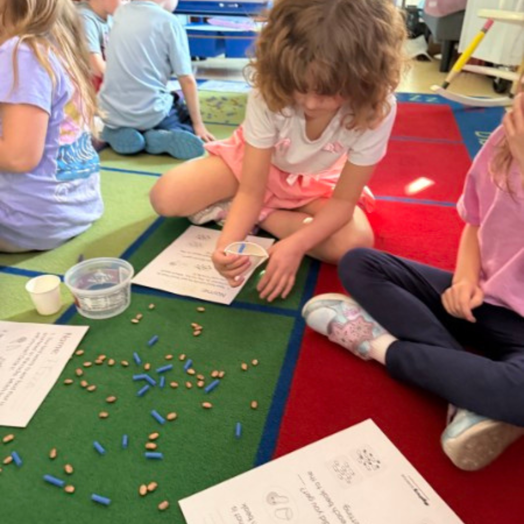Four students gathered in a circle on a classroom rug, working together on an interactive activity.