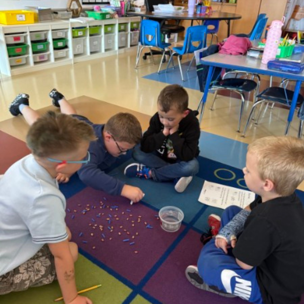 A student sitting on the classroom carpet, participating in a hands-on activity with paper cups and worksheets