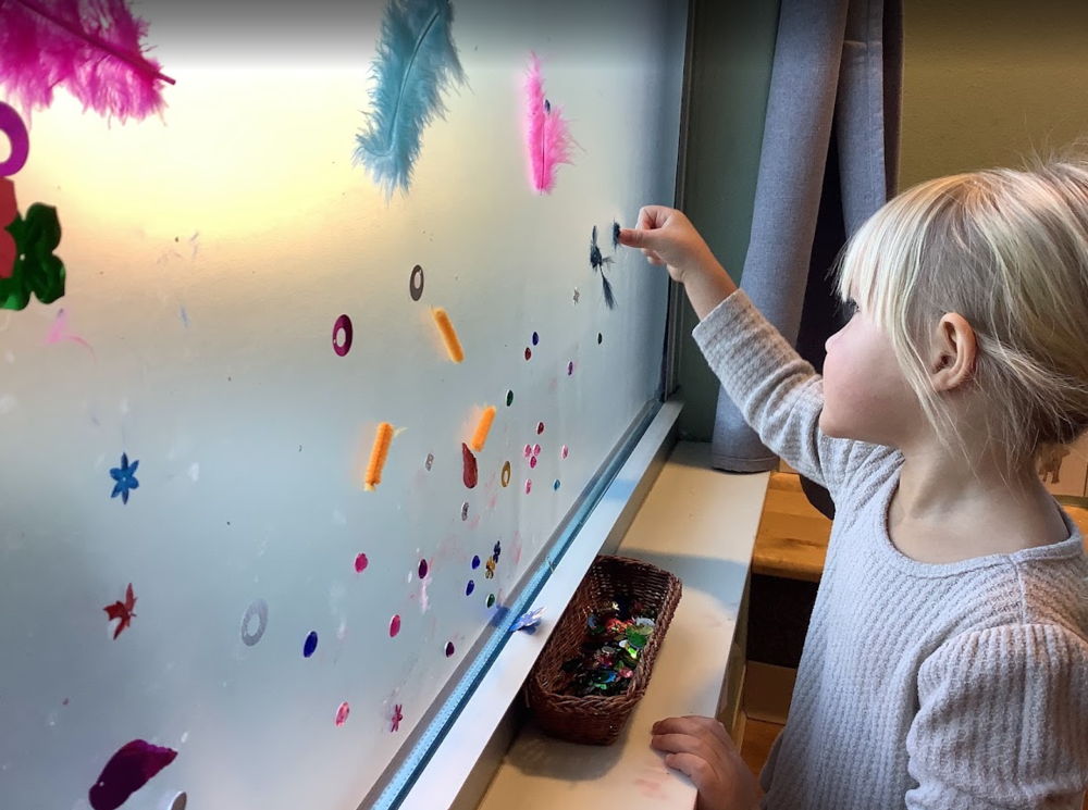 An ECC students sticks treasures to sticky paper on the window in her classroom.