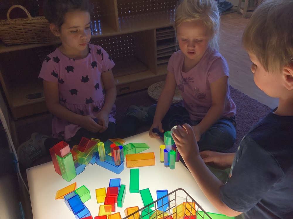 Children sit around a light table playing with translucent colored shapes. 