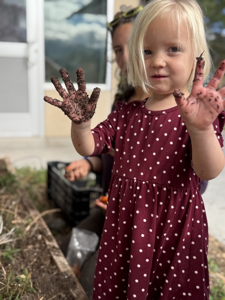 An ECC student shows her hands to the camera after planting some yarro in the garden bed on the playground.