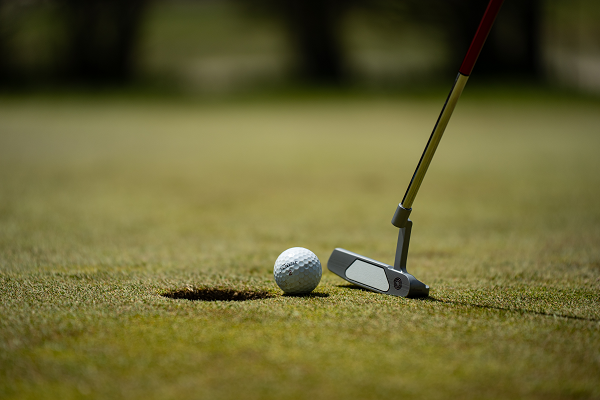 Golf Ball balanced on the edge of the hole in front of a golf club on the green