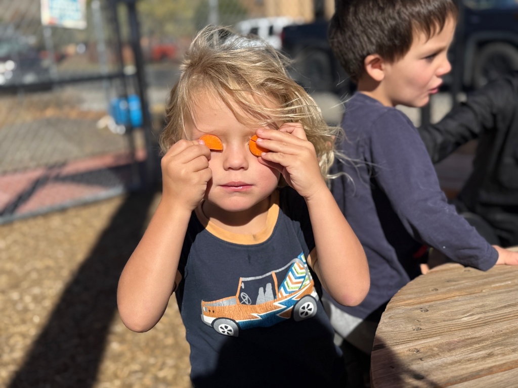 A preschool student covers his eyes with cut carrots.