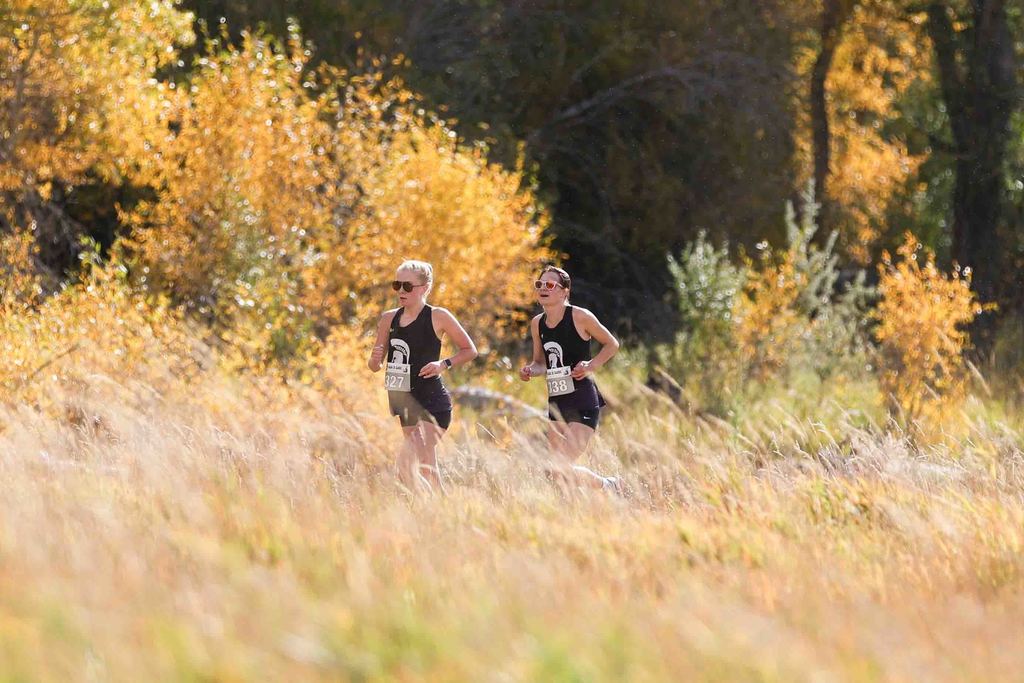 Two girls cross country runners running through the autumn colors at the home meet at Vanderveer Ranch