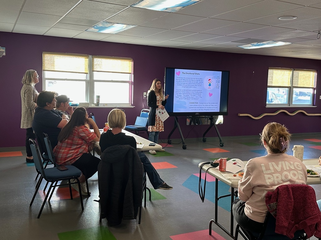 SECC Parents sitting in chairs in the gym listening to a staff member share information about Conscious Discipline. 