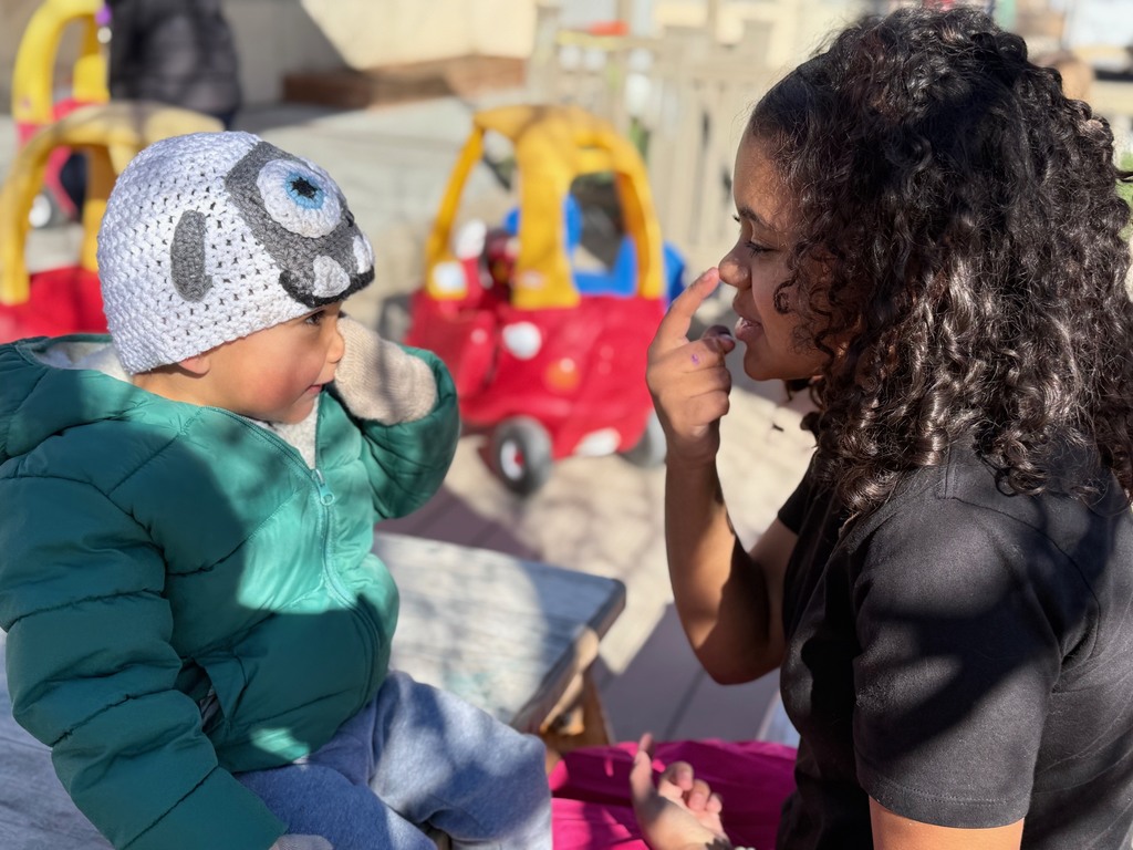 A preschool student and a middle school student facing each other and pointing to their noses.
