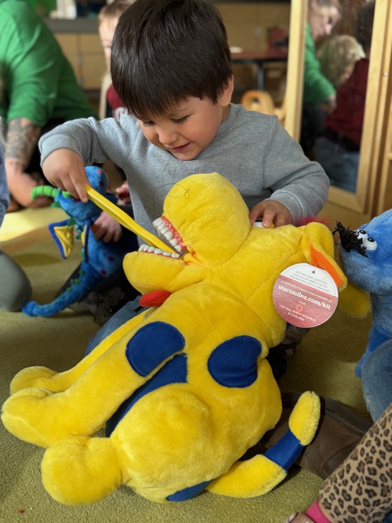 An ECC student practices by brushing a stuffed animals teeth with a toothbrush.