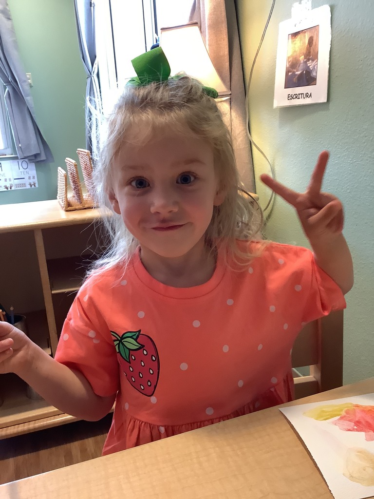 A ECC student flashes a peace sign while sitting at a table in her classroom. 