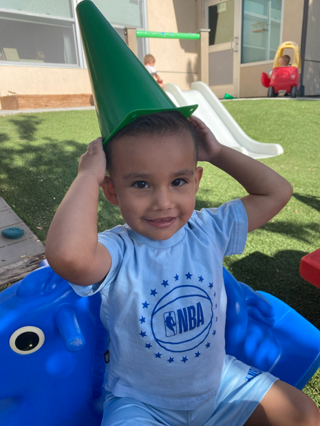 An ECC student wears a green cone on his head on the playground. 