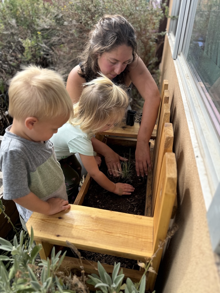 A couple of toddlers help plant chives in the new planter on their playground. 