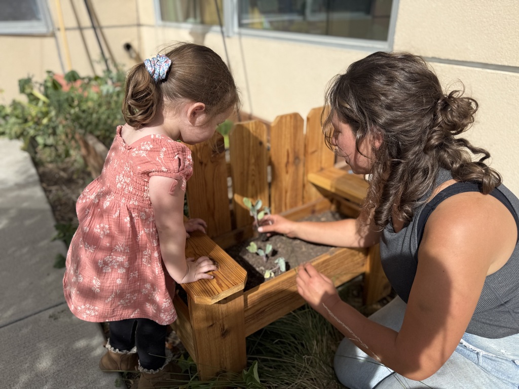 A SECC student helps Maytal from Guidestone plant a vegetable starter in the new planter on the playground. 