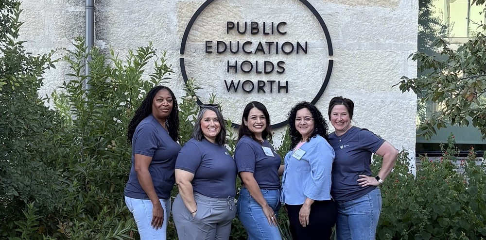 Five women stand in front of sign saying Public Education Holds Worth