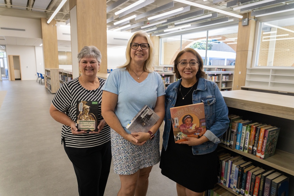 three women hold books in library