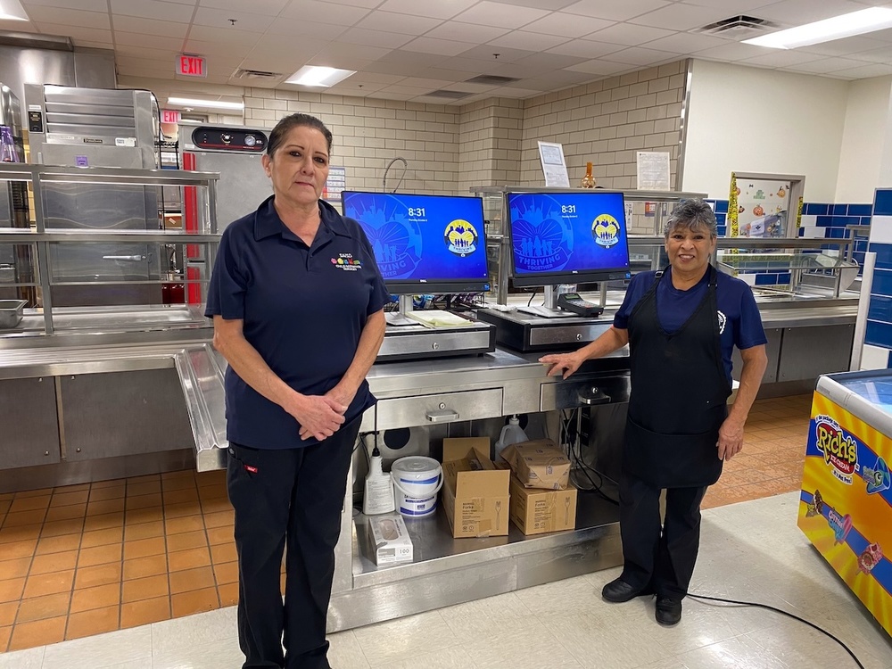 Two women stand in front of cafeteria equipment