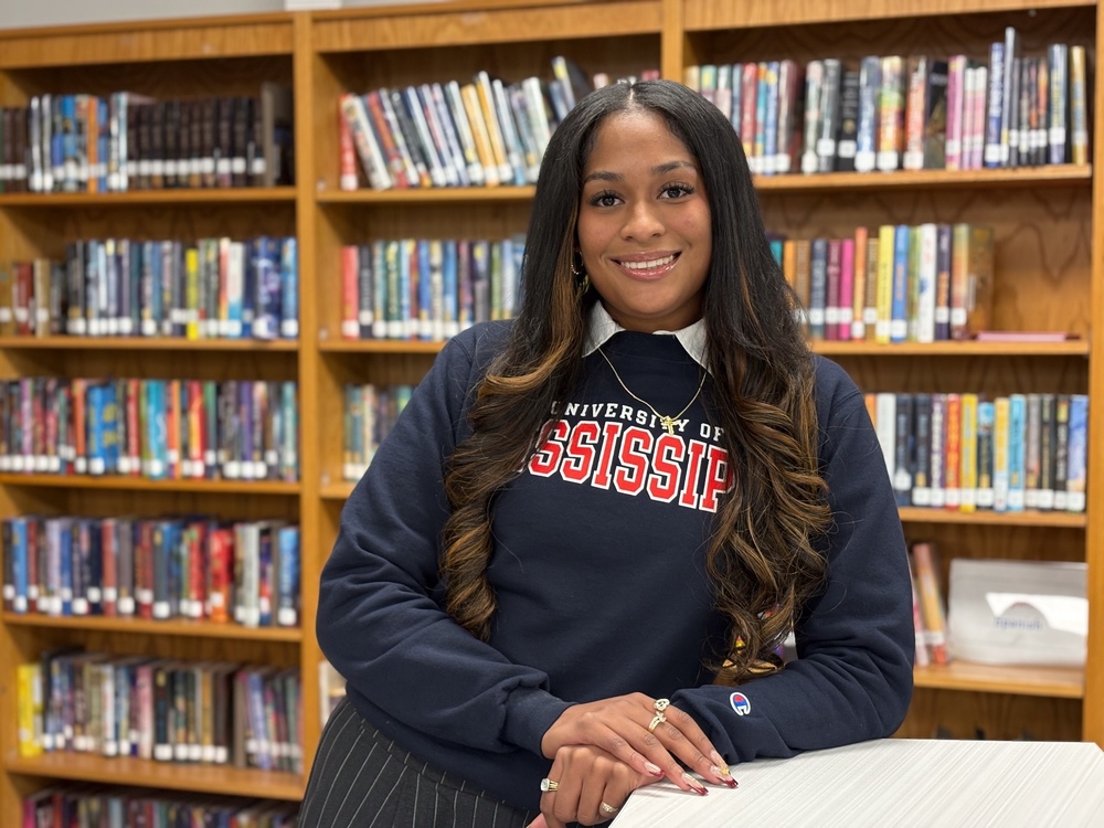 Ms. Cook stands in front of bookcase
