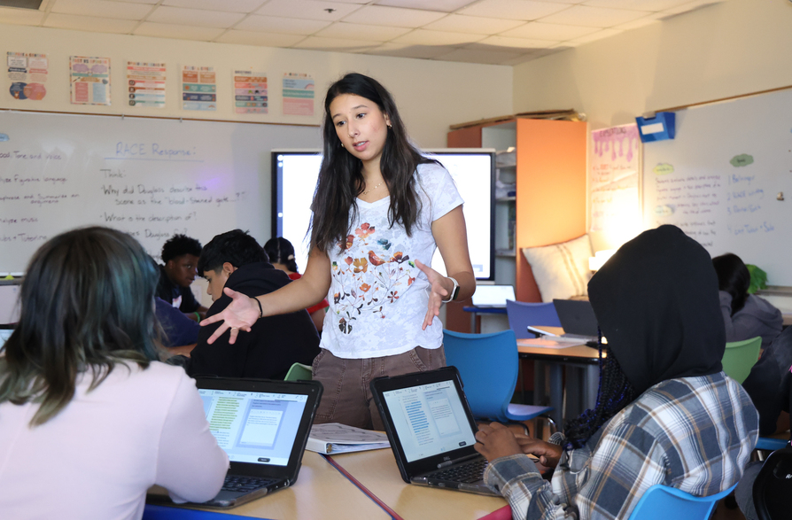 Teacher instructing two students with laptops