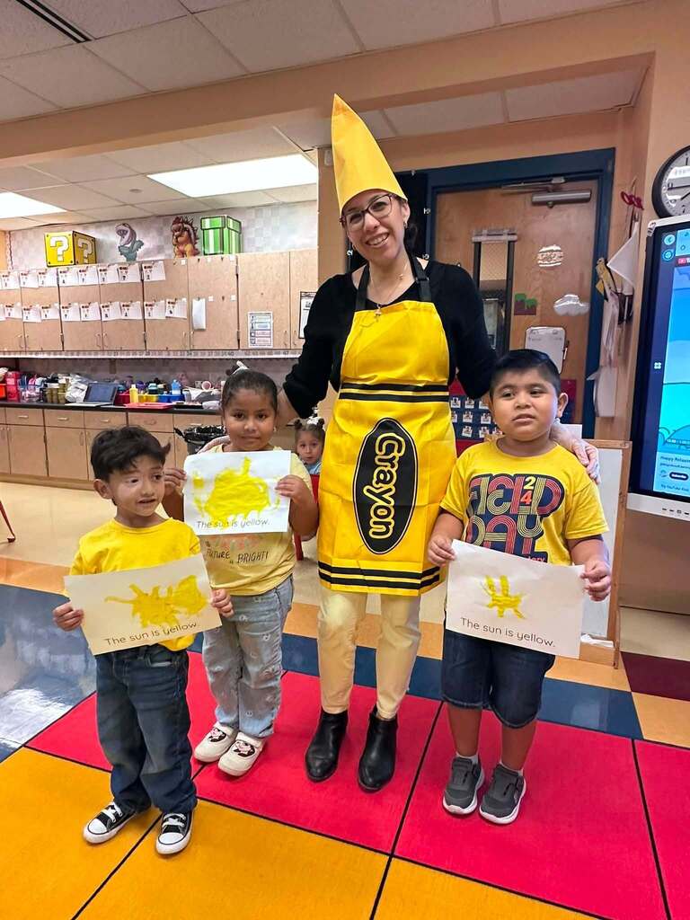 kids posing with a person in a yellow crayon costume with their yellow sun artwork