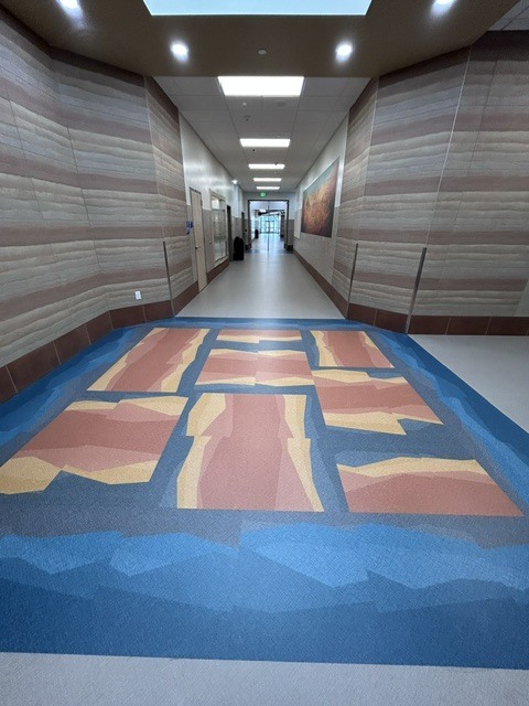 Long hallway with striped walls and a colorful floor design. The floor has blue, orange, and yellow patterns.