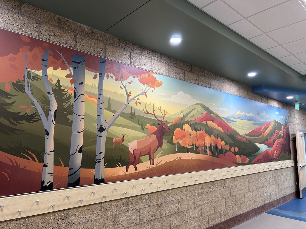A large mural of a forest with birch trees, an elk, and a deer is on a brick wall.
