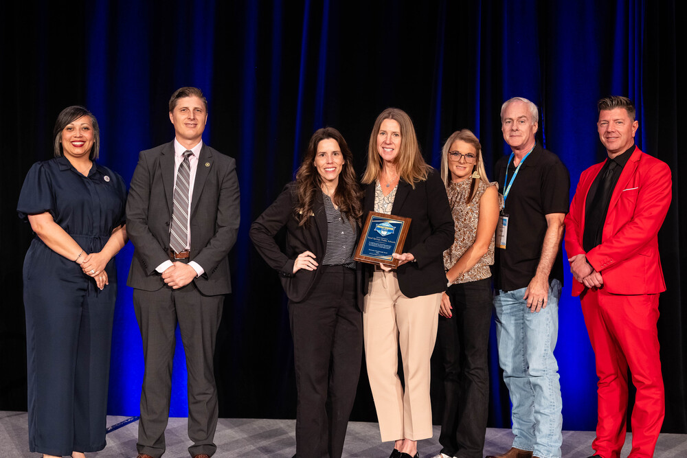 Superintendent Sherry Durkee and Executive Director of Compliance Angelia Noel hold a plaque recognizing Sand Springs Public Schools as a “2026 OPSRC Breakthrough School” while presenters pose together to celebrate the achievement.