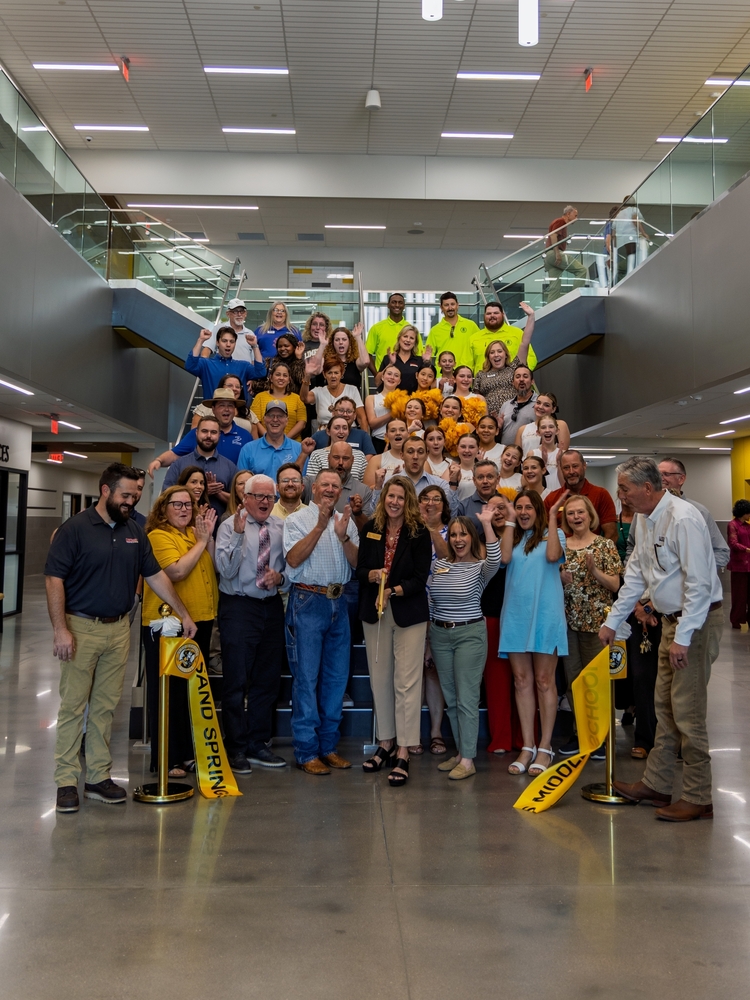 Staff and community members celebrate at a ribbon-cutting ceremony on a modern school staircase with Sand Springs Middle School banners.