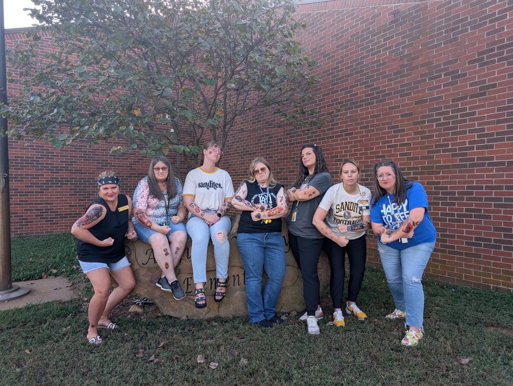 Angus Valley staff poses in front of the school, showing off temporary tattoos.