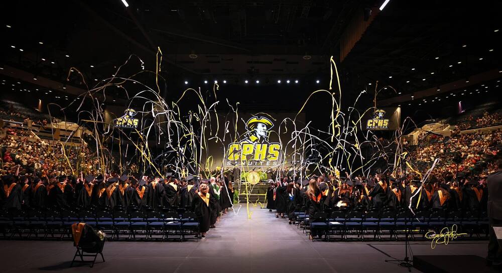 Graduation commencement with yellow and white streamers flying in the air.