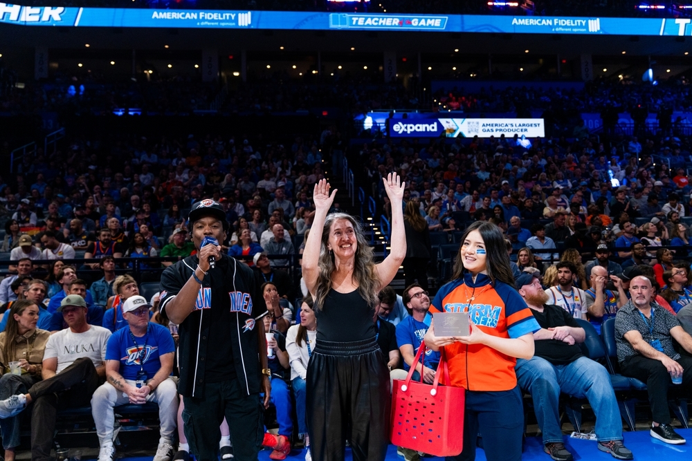 Teacher Lisa Wolf stands in front of a packed stadium and waves to people in the stands.