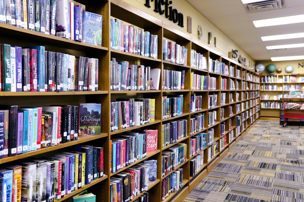 Long book shelf filled with books in high school library. Wall art with text reading "fiction".