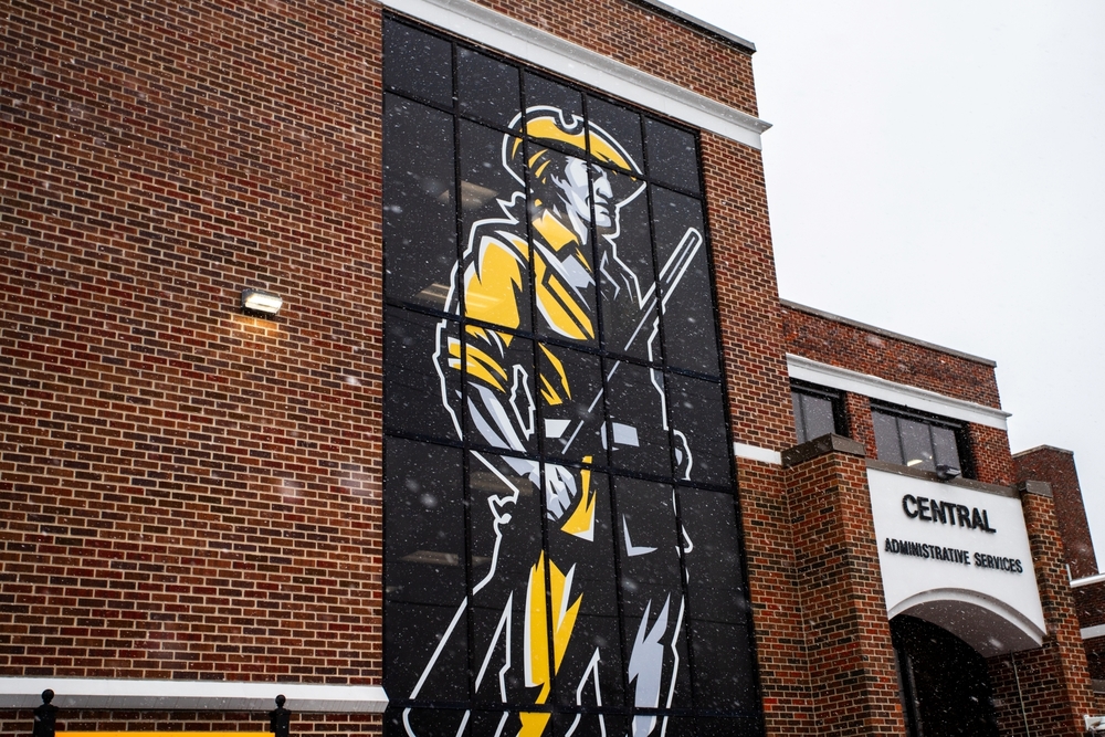 Snow falls outside the Sand Springs Public Schools Central Administrative Services building with a large Sandite mural.