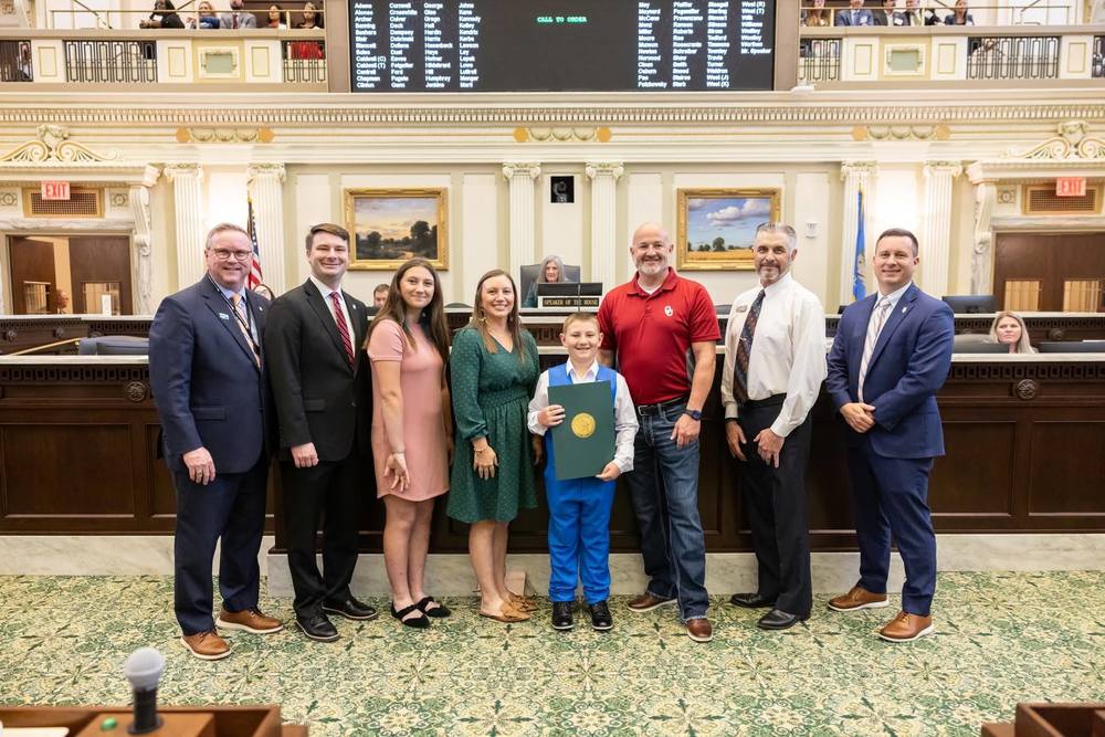 Elementary student at the Oklahoma State Capitol, holding a citation, and surrounded by his family and legislators.