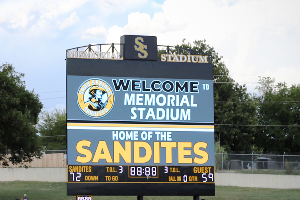 Video scoreboard with Sand Springs interlocked S logo. Text displayed reading "Welcome to Memorial Stadium. Home of the Sandites"