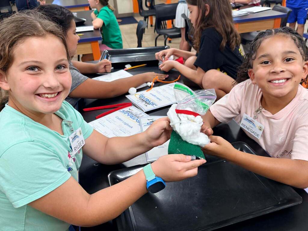 Two smiling students holding a handmade craft with cotton and felt, sitting at a desk during a STARBASE STEM activity.  Image 2