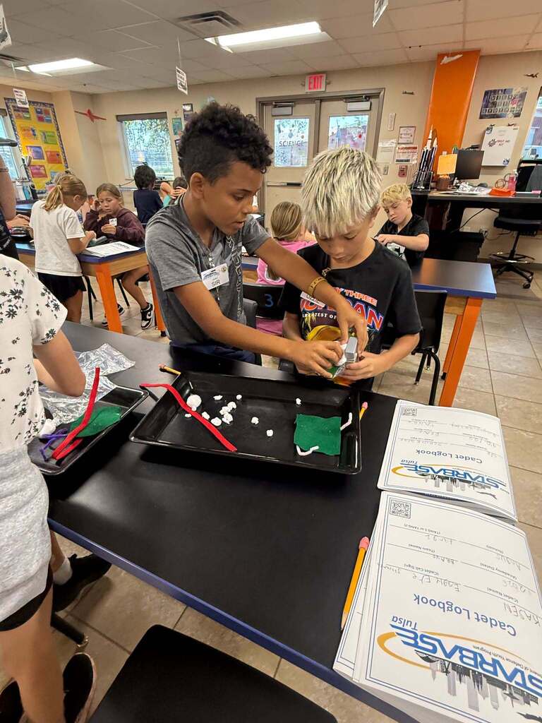 Two students work together on a hands-on project at a lab table while referring to their STARBASE Cadet Logbooks.