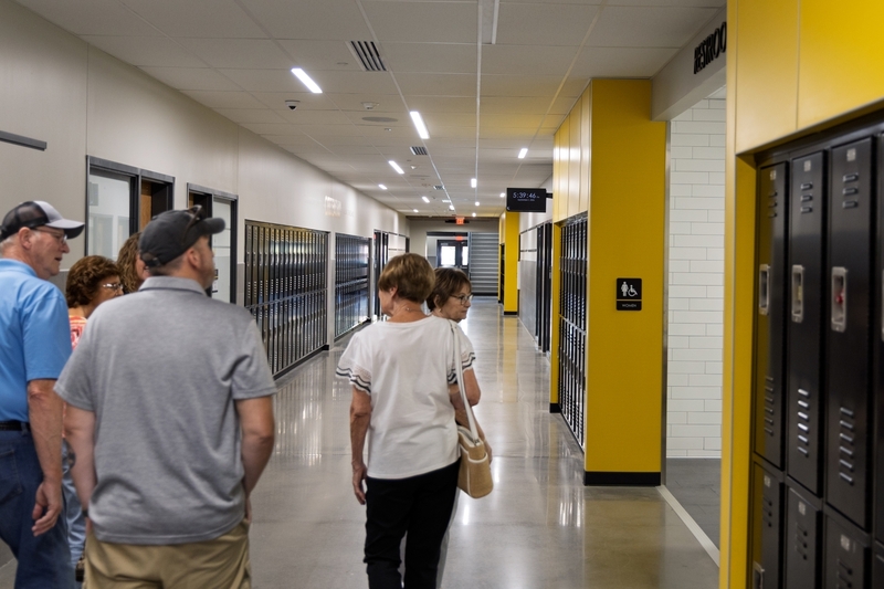 People walk away down a bright, modern school hallway lined with grey and yellow walls, black lockers, and polished concrete floors.