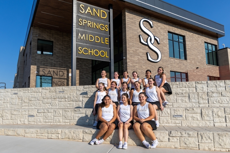 A group of twelve middle school students wearing matching athletic uniforms pose together on stone steps outside Sand Springs Middle School.