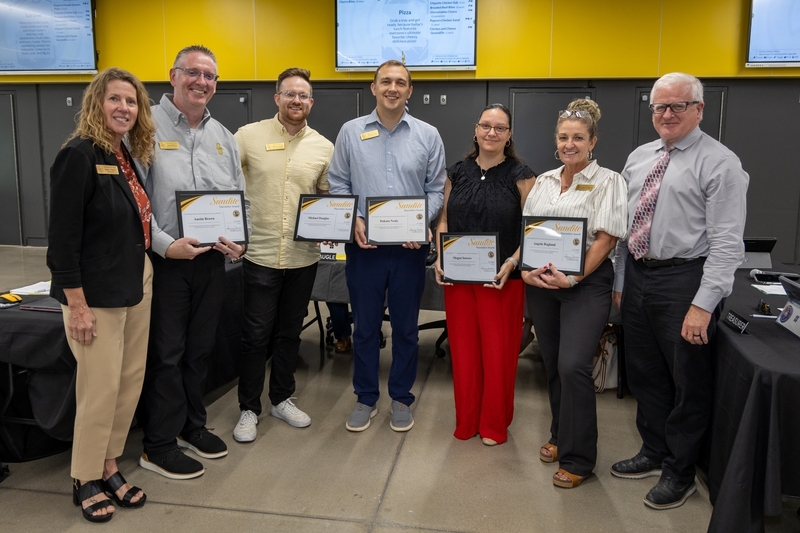 A group of five award recipients hold framed Sandite certificates and stand next to Superintendent Durkee and Board President Mike Mullins.