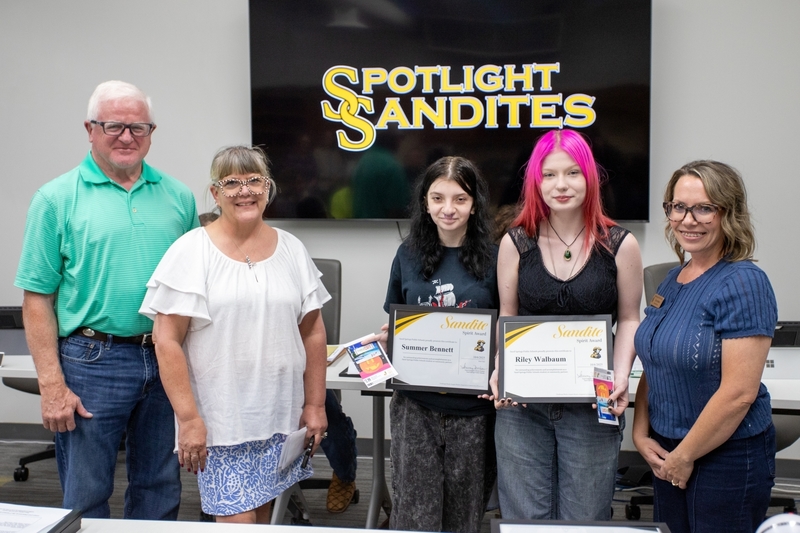 Two page academy students receive certificates for the Sandite Spirit Award. They are standing next to board members and a Page Academy teacher.