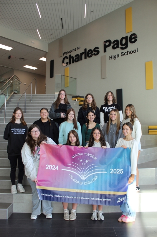 A group of High School yearbook students stand on the main staircase holding a colorful banner that reads “National Yearbook Program of Excellence 2024–2025, Gold Level.” The “Welcome to Charles Page High School” wall sign is visible behind them.