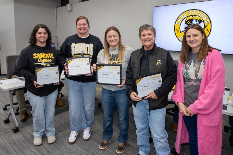 Lady Sandite coaches stand together at a Board of Education meeting, holding Sandite Spirit Award certificates.