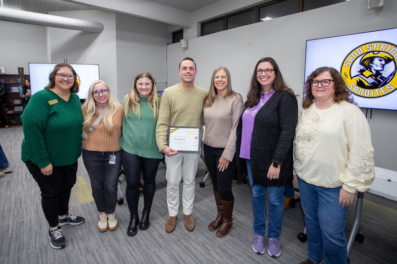 A group of Daybreak staff stands together at a Board of Education meeting as one staff member holds a Sandite Pacesetter Award certificate.