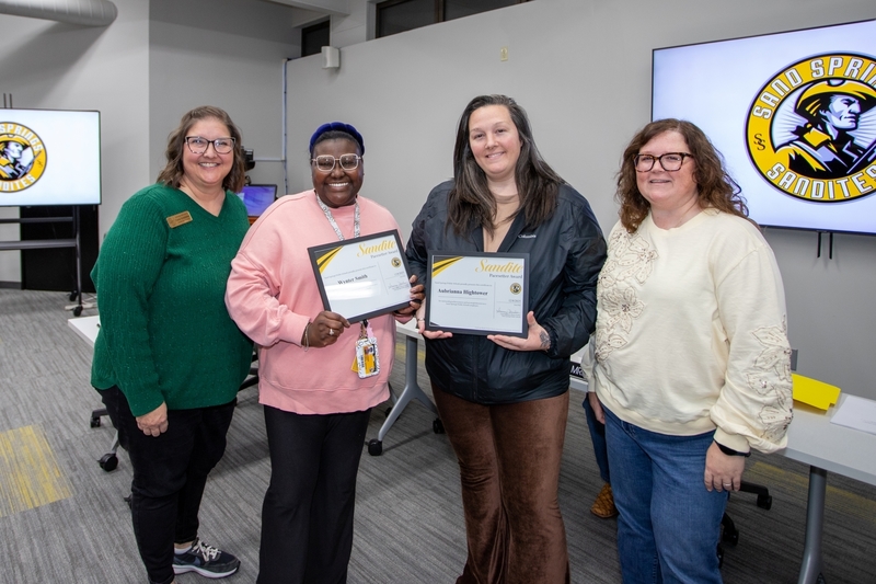 District leaders pose with two recipients holding Sandite Pacesetter Award certificates at a Board of Education meeting.