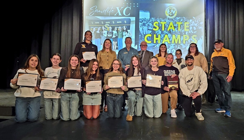 Sand Springs cross country athletes and coaches pose on stage holding certificates during the January 2026 Sand Springs Board of Education Meeting