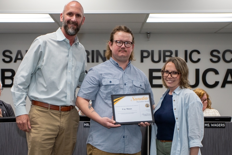 Speech and debate coach Coy Moses receives certificate of recognition from school administrator and board member.