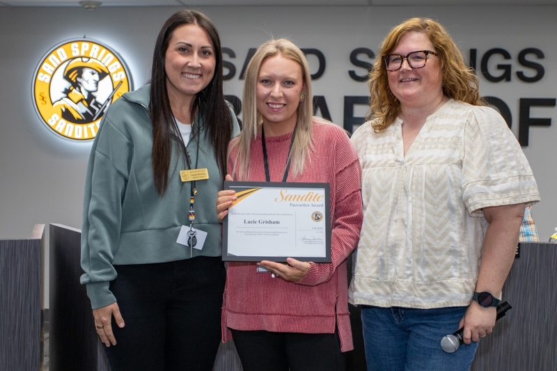 Lacie Grisham receives certificate of recognition from school board member and official.