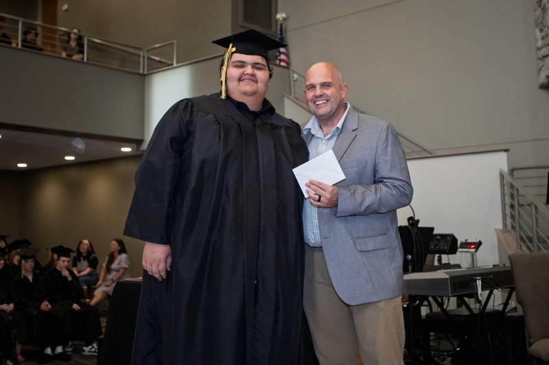 Principal Jay Rotert presents student in graduation cap and gown with an envelope.