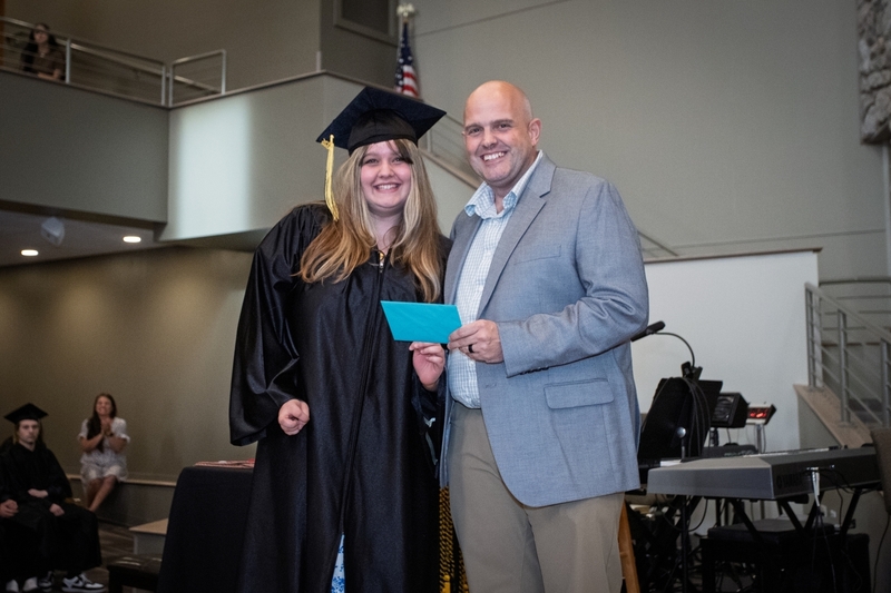 Principal Jay Rotert presents student in graduation cap and gown with an envelope.