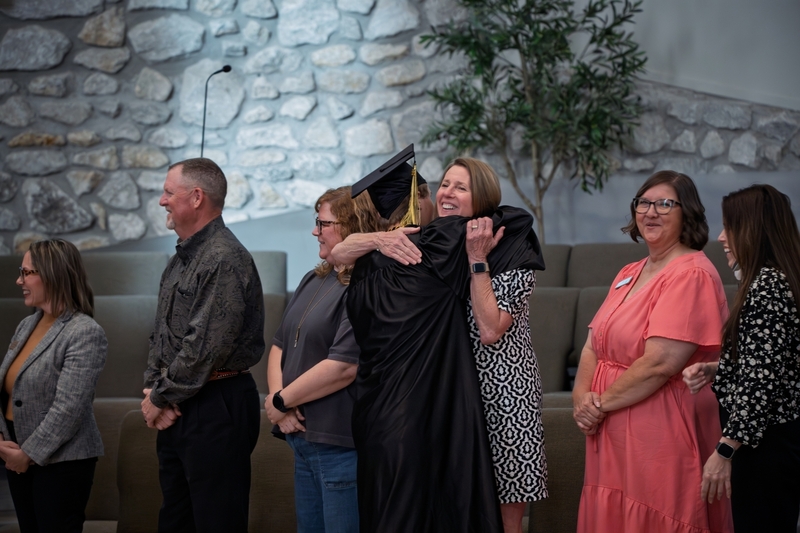 Superintendent Sherry Durkee hugs a student in graduation cap and gown on stage.