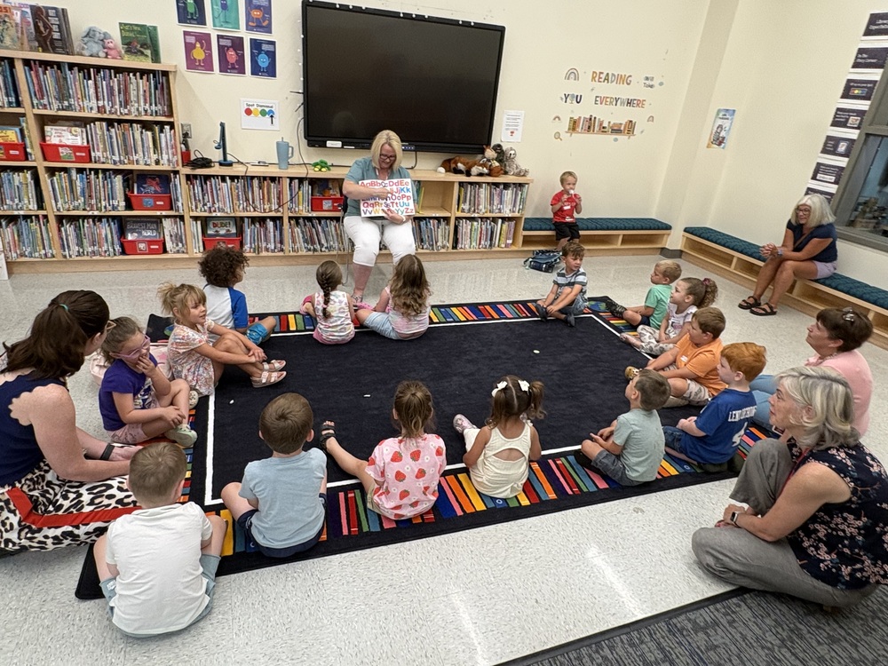 Children sitting in a circle on a rug during a read-aloud.